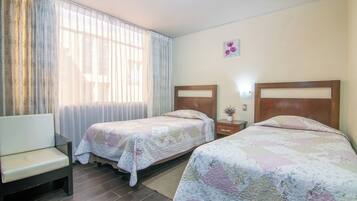 Una habitación de hotel con dos camas, un sofá, un ventanal con cortinas y un pequeño adorno en la pared.