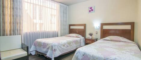 A hotel room with two beds, a sofa, a window with curtains, and a small wall decoration.