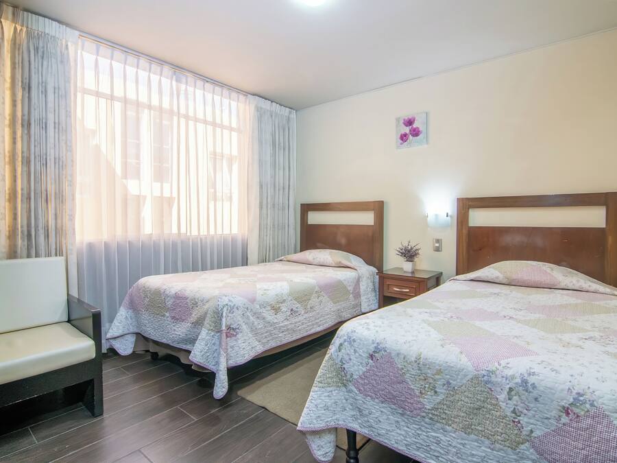 Una habitación de hotel con dos camas, un sofá, un ventanal con cortinas y un pequeño adorno en la pared.