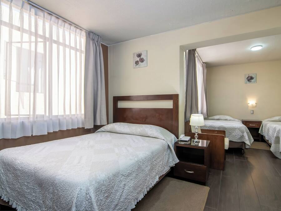 A hotel room with a large bed, two smaller beds, a desk with a lamp, and a nightstand.