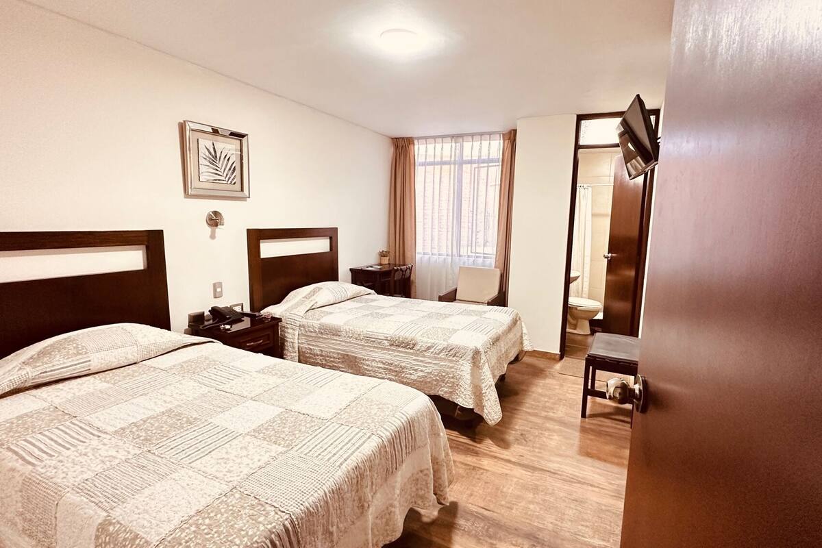 A hotel room with two beds, a desk, a chair, a mirror, and a window with curtains.