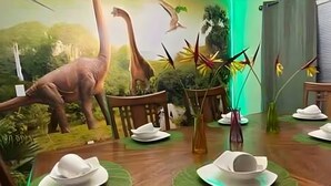 Une table à manger dressée avec de l’argenterie et des assiettes blanches, entourée d’une fresque représentant des dinosaures et de la végétation.