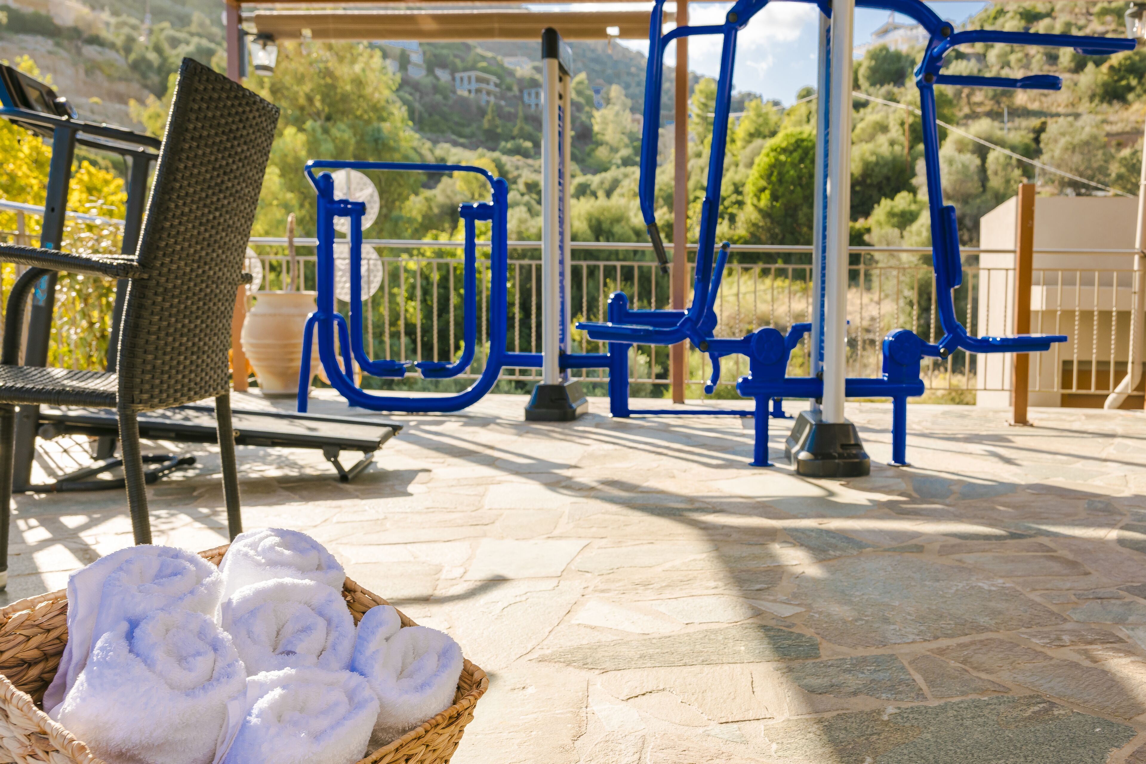 An outdoor exercise area with a chair, a basket of towels, and exercise equipment.