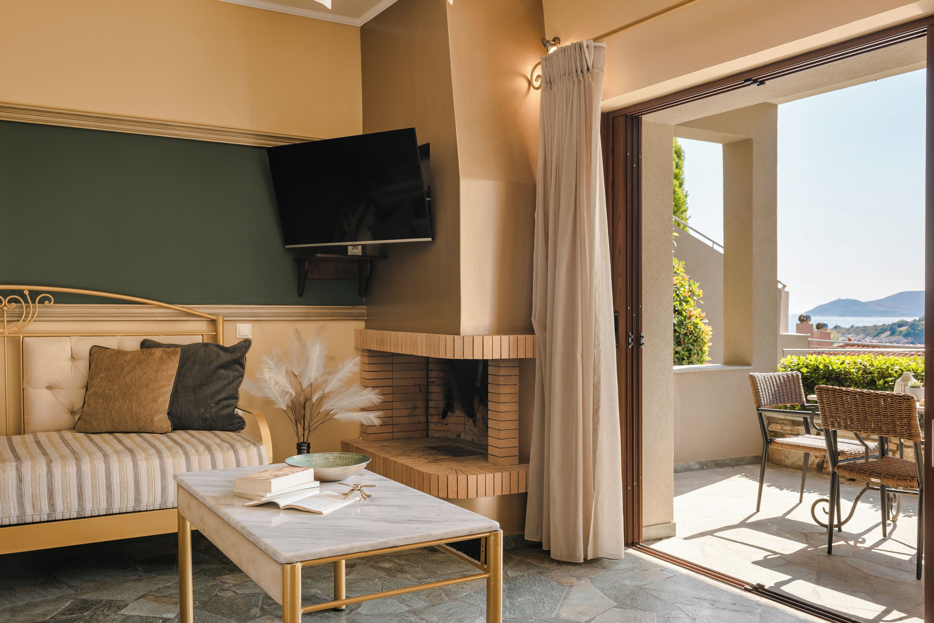 A cozy living room with a sofa, a flat-screen TV, a fireplace, and a balcony with wicker furniture.