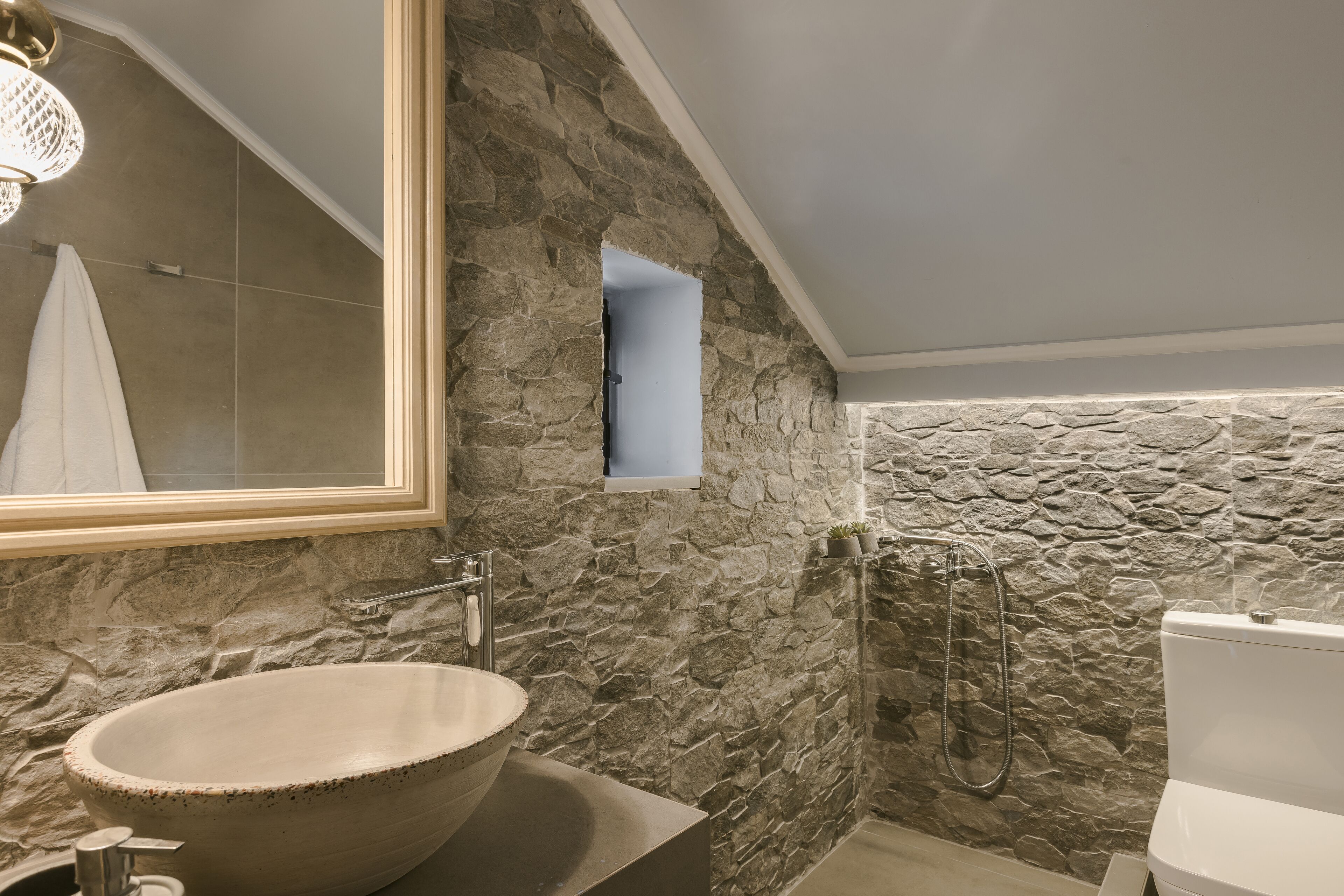 Un bagno con parete in pietra, un lavabo ampiamente dimensionato, un soffione doccia a mano e un water.