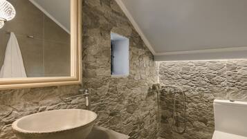 Un bagno con parete in pietra, un lavabo ampiamente dimensionato, un soffione doccia a mano e un water.
