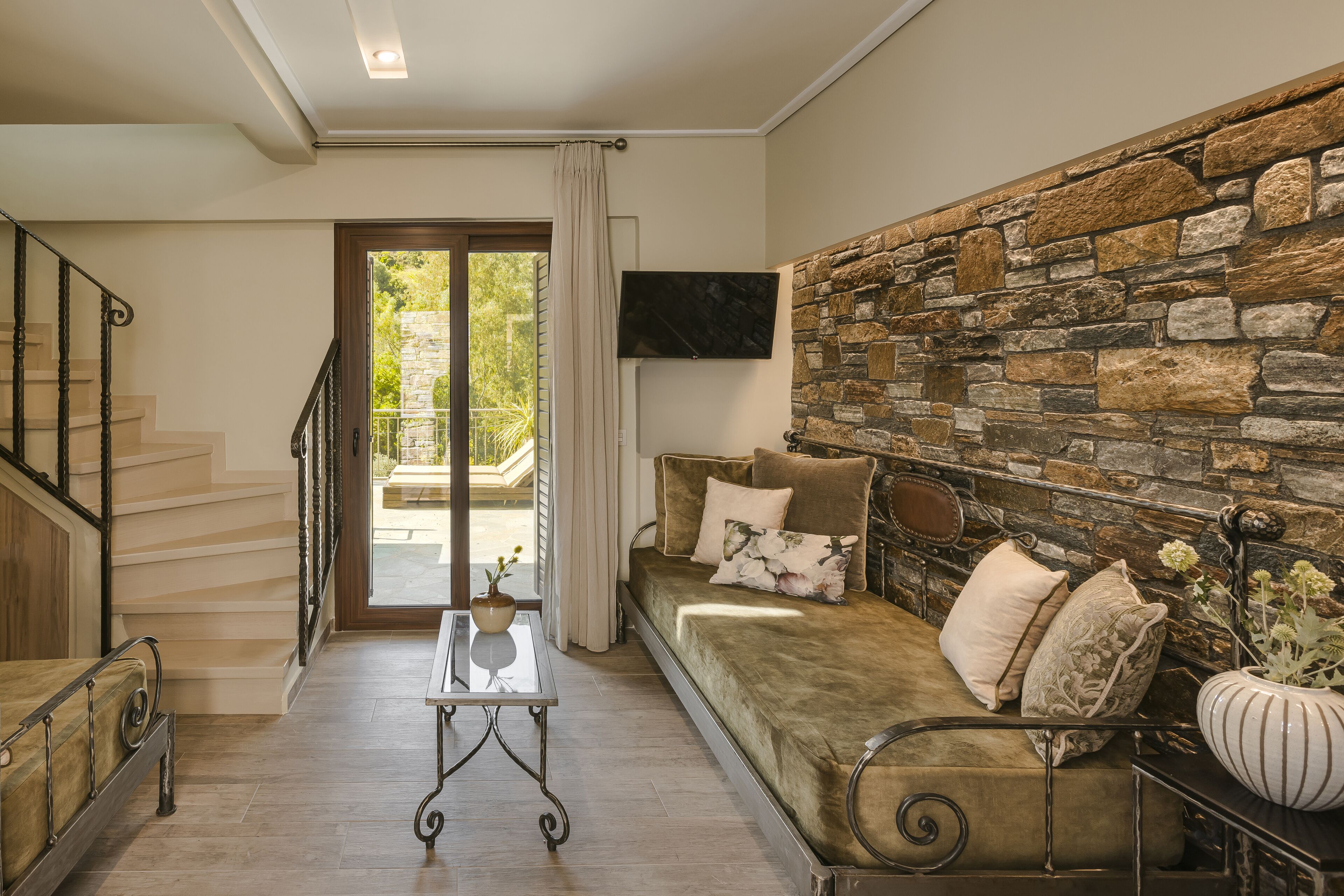 A living room with a stone wall, a sofa with cushions, a coffee table, and a TV mounted on the wall.