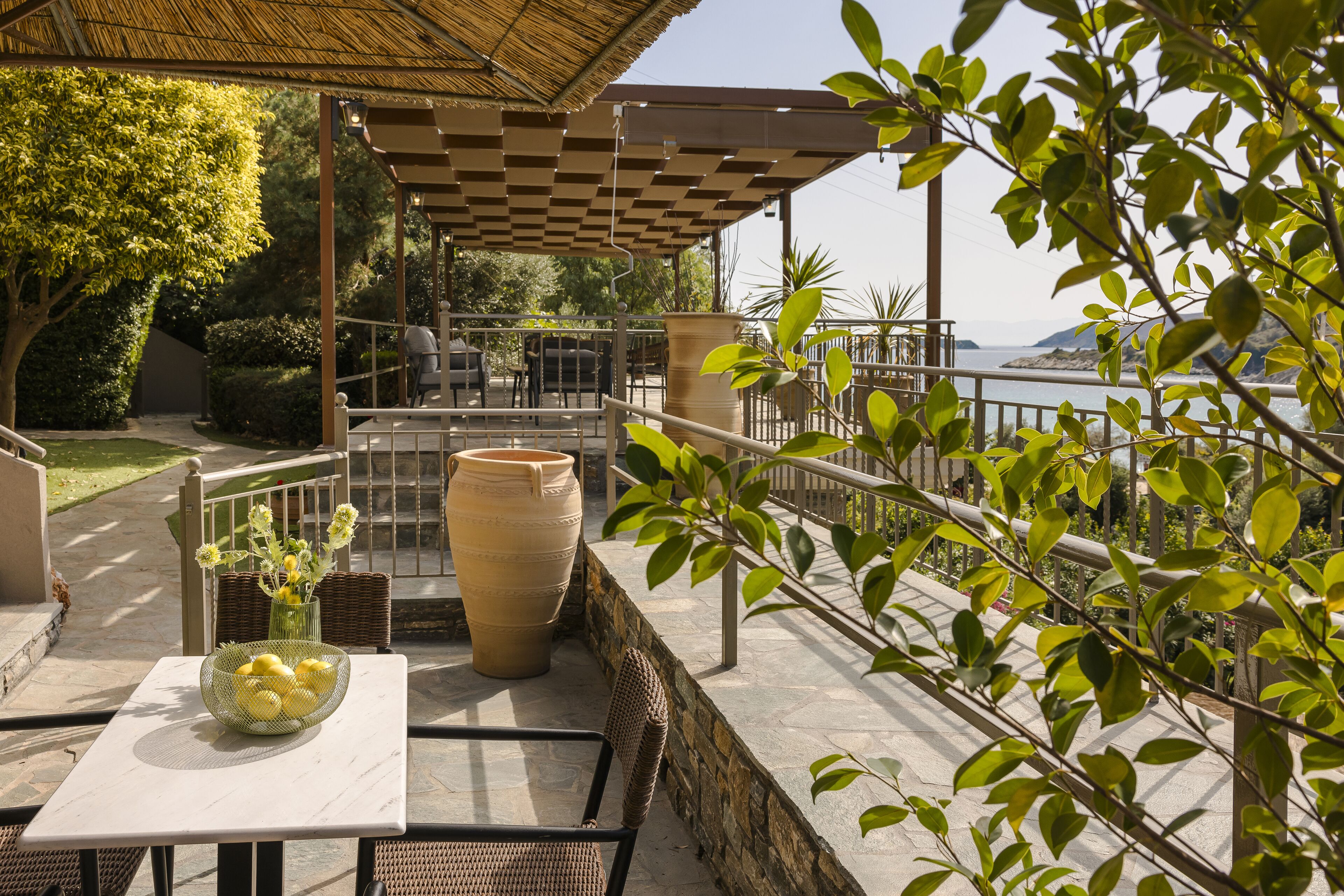 An outdoor patio with a table, chairs, a large vase, and a view of the sea.