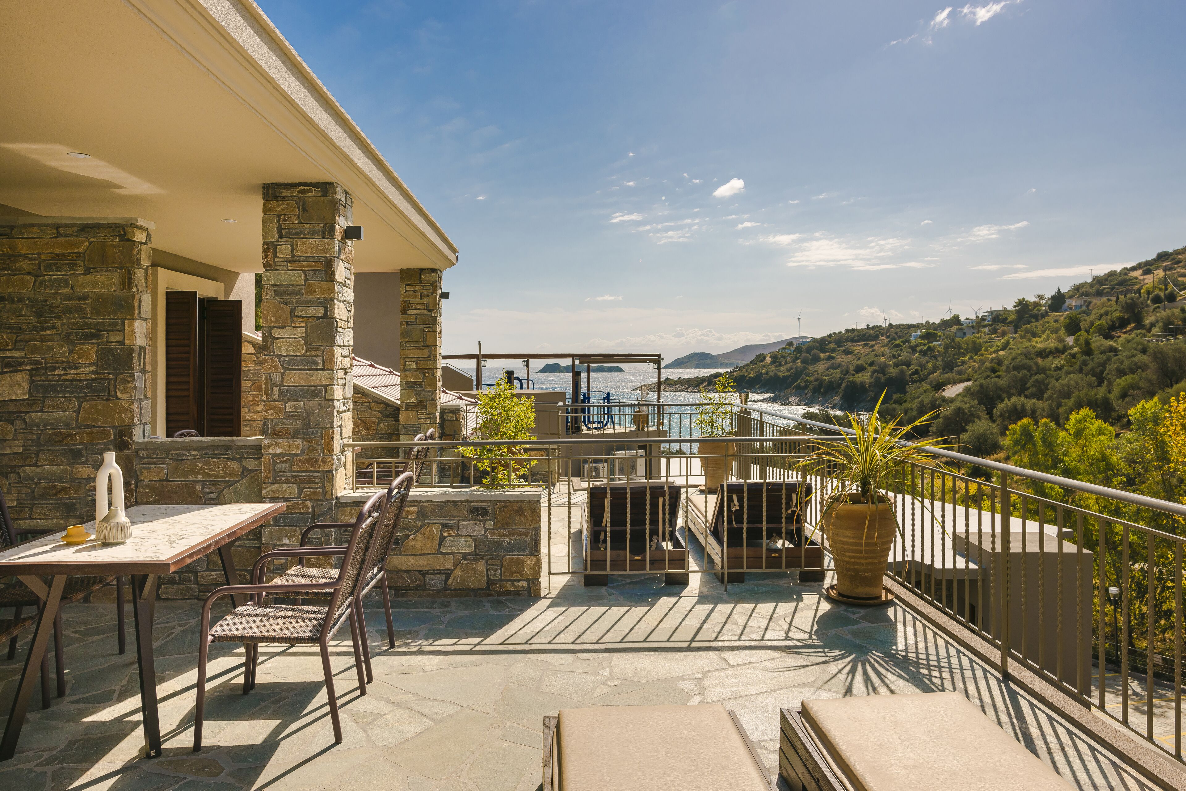 A balcony with stone walls, a table, chairs, and a potted plant.