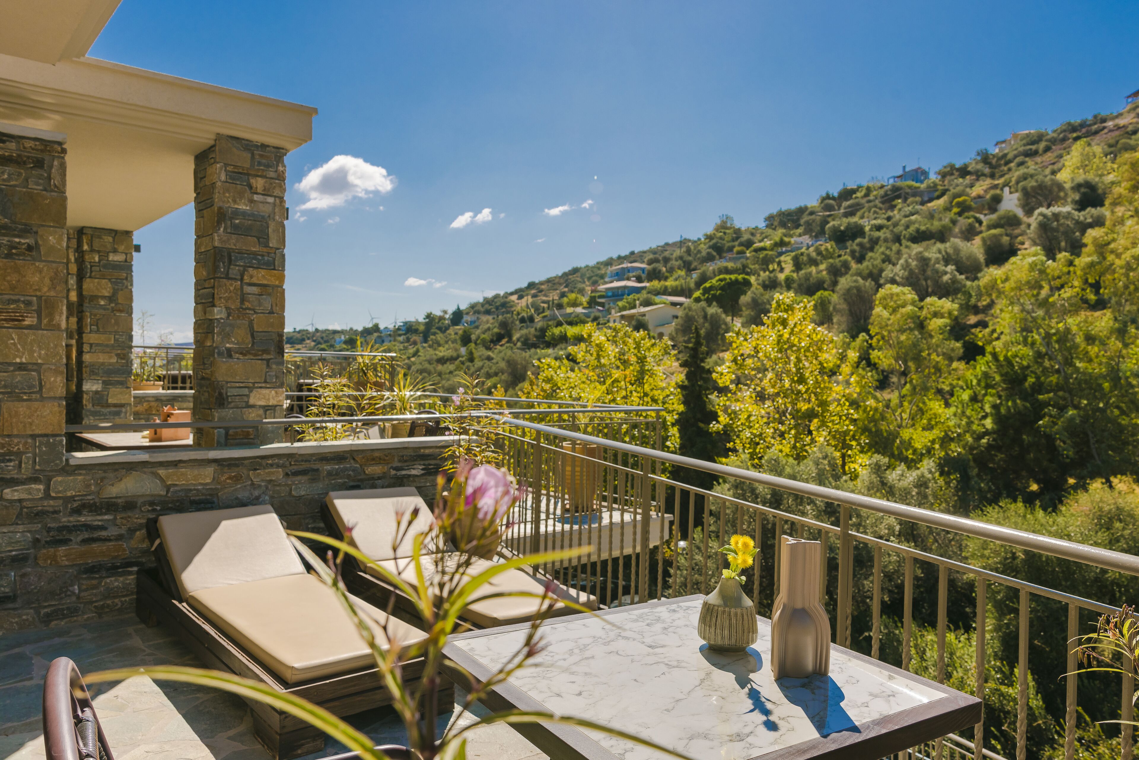 A balcony with stone pillars, a table with a vase, and lounge chairs.