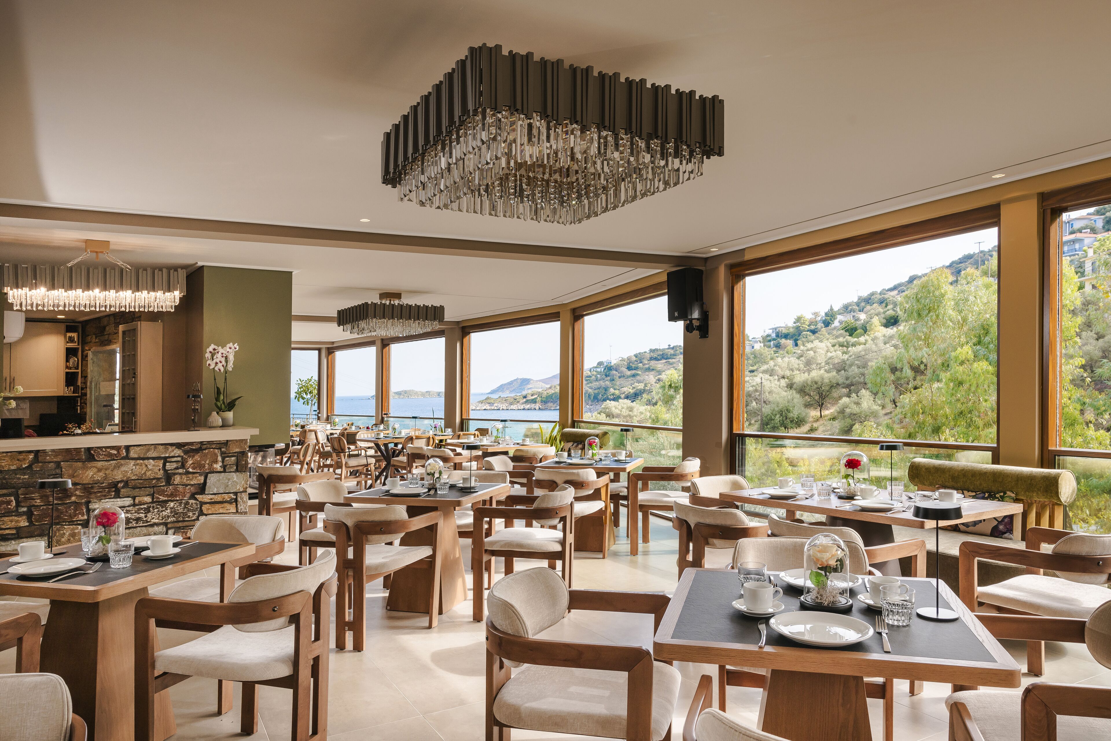 Un comedor amplio con varias mesas y sillas, ventanas grandes que ofrecen vistas panorámicas y una lámpara moderna.