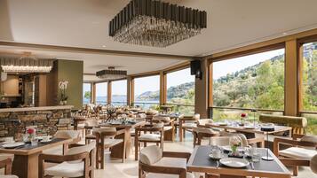 Un comedor amplio con varias mesas y sillas, ventanas grandes que ofrecen vistas panorámicas y una lámpara moderna.