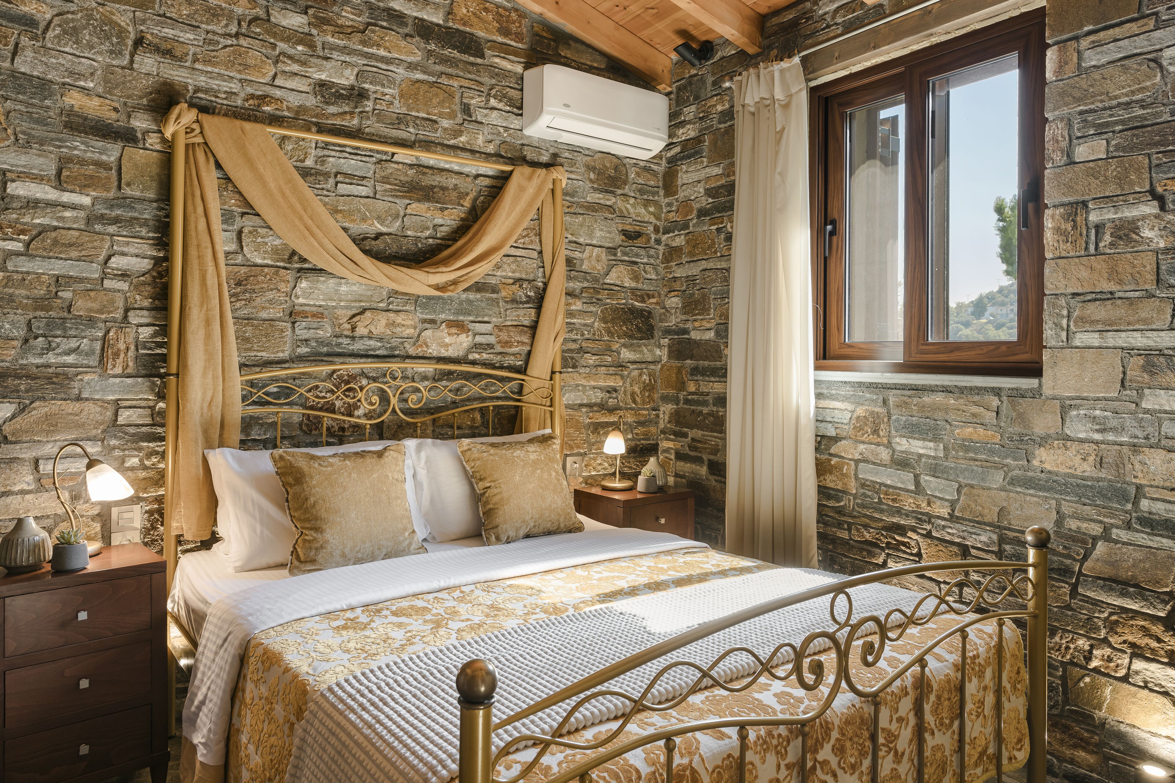 Un dormitorio con paredes de piedra, una cama, cortinas y una ventana.