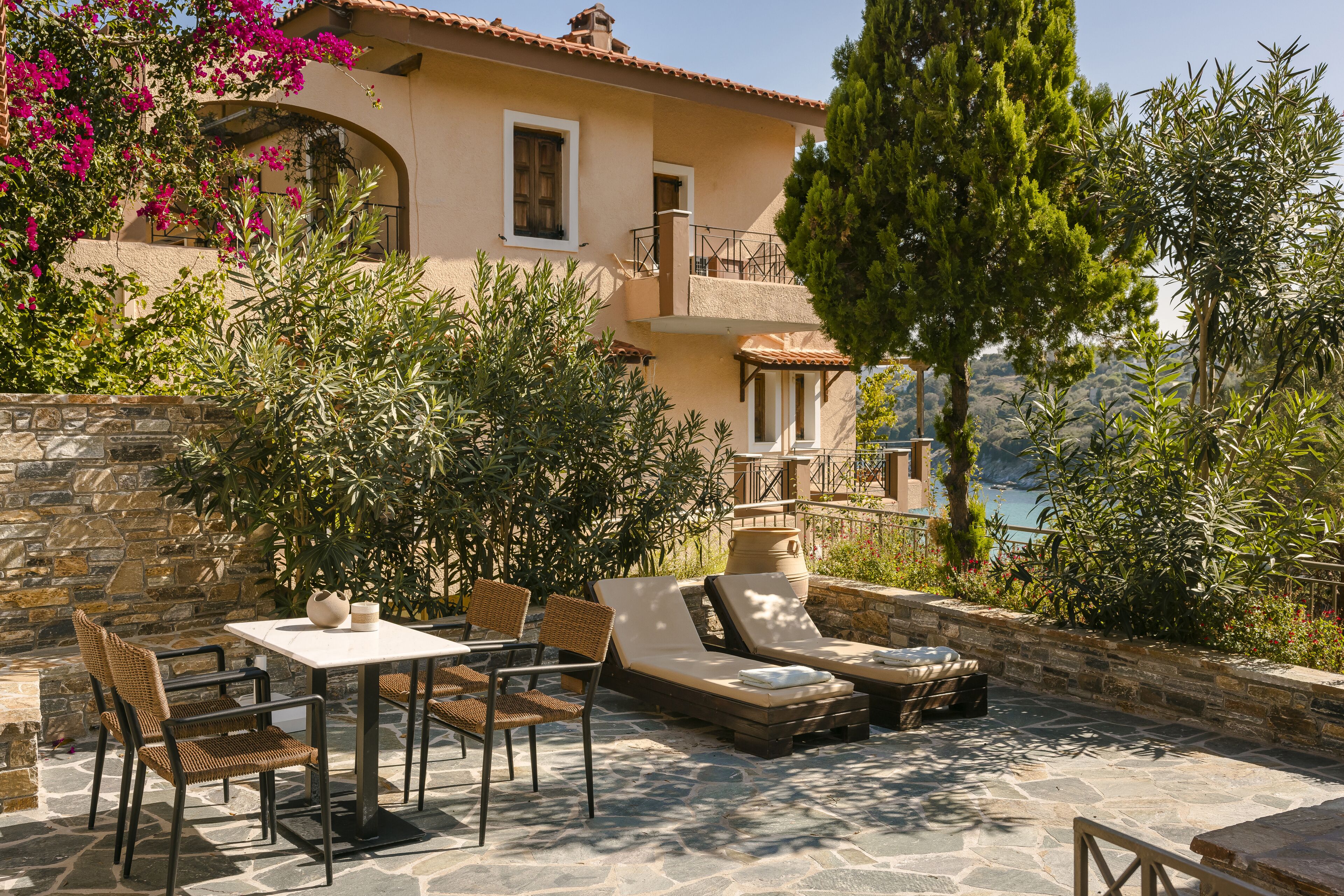 Une terrasse extérieure avec un sol en pierre, une table avec des chaises et des fauteuils de jardin.