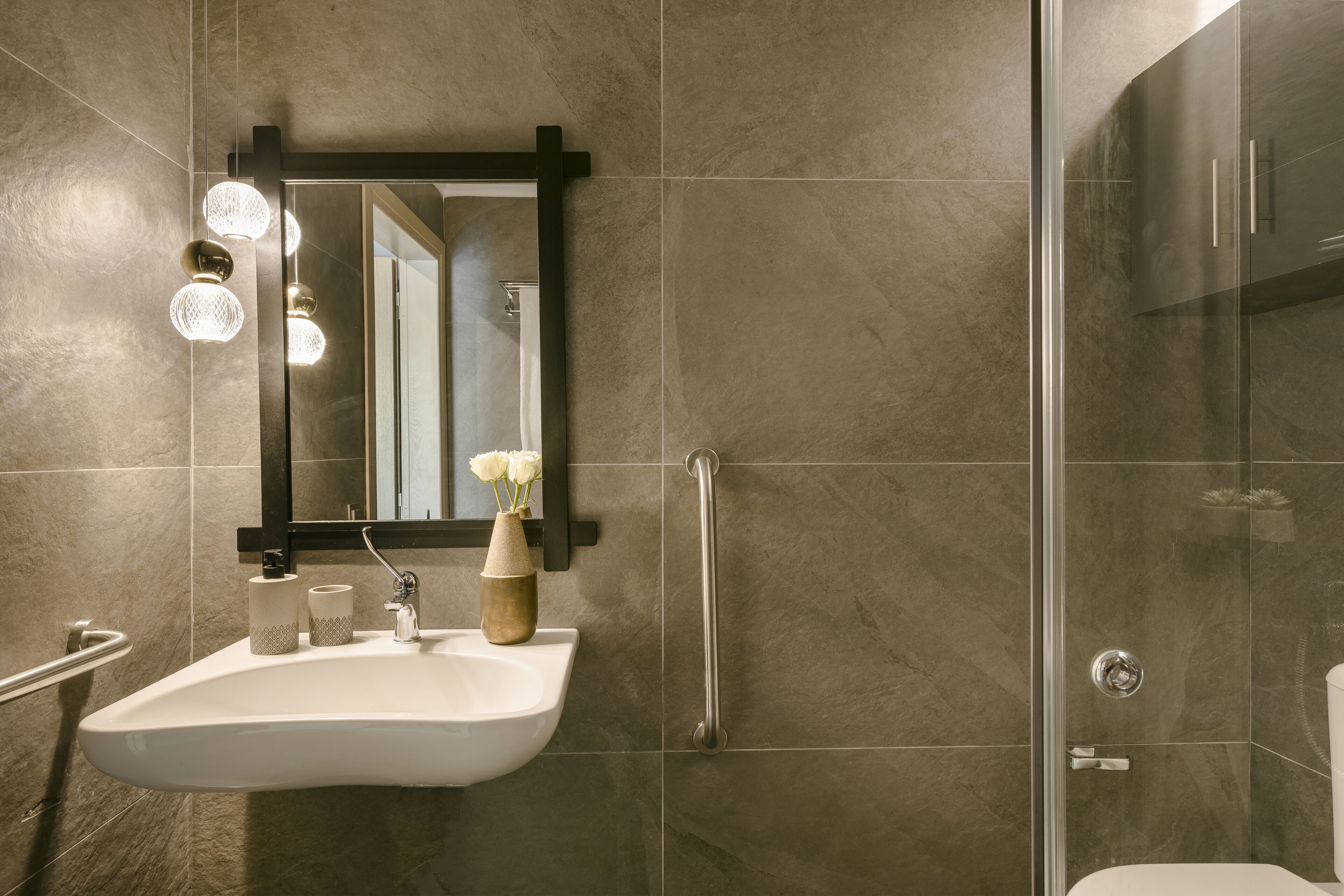 Un baño moderno con lavamanos blanco, un espejo y cabina de ducha.