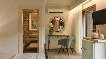 A compact hotel room with a bed, a small desk with a chair, a kitchenette, a bathroom with a stone wall, and a TV.
