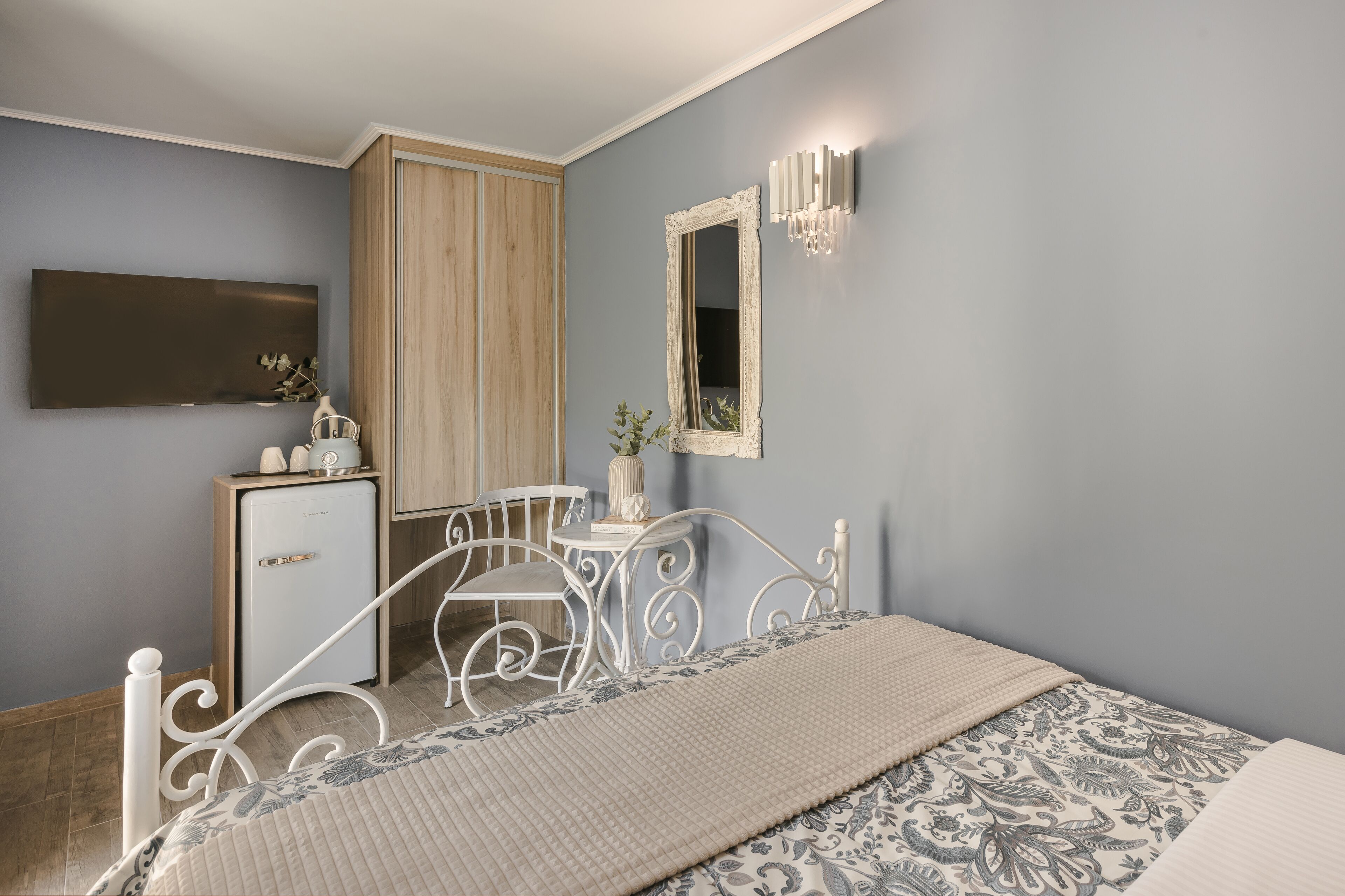 A bedroom with a bed, bedside table, dresser, mirror, and wall-mounted light fixture.