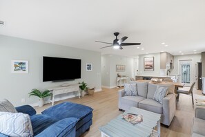 A modern living room with a flat-screen TV, a ceiling fan, and a dining area with a table and chairs.