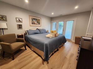 Ein Schlafzimmer mit einem Bett, einem Sessel, einem Schreibtisch und einem Fenster mit Jalousien.