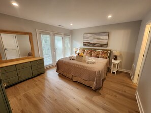 Un dormitorio con cama, cómoda, espejo, ventana con persianas y un cuadro en la pared.