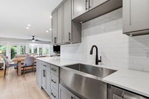 A modern kitchen with a stainless steel sink, grey cabinets, and a white tiled backsplash.
