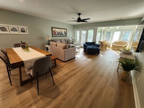 Ein geräumiger Wohnbereich mit Esstisch, Sofa und Sesseln, Deckenventilator und großen Fenstern.