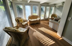 Ein sonnendurchflutetes Zimmer mit Korbmöbeln, einem gestreiften Sofa und einem Deckenventilator.