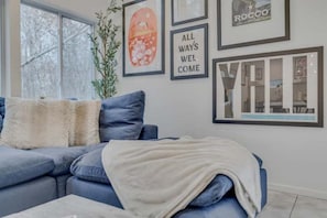 A modern living room with a blue sofa, a white throw blanket, and framed artwork on the wall.