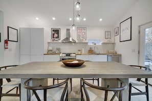 A modern kitchen with a wooden table, white cabinets, and a hanging light fixture.