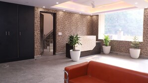 A modern lobby with a reception desk, potted plants, a staircase, and a red sofa. - Lyf Corporate Suites - Noida Sector 19 (Noida)