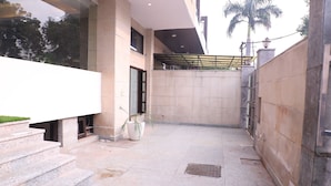 A modern building with a stone facade, a covered outdoor area with steps, and a palm tree in the background. - Lyf Corporate Suites - Noida Sector 19 (Noida)