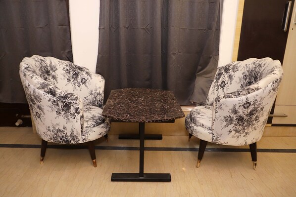 Una habitación con dos sillones tapizados de estampado floral, una mesa cuadrada con tapa de diseño oscuro y una lámpara de pie oscura.