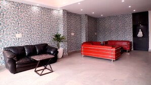A modern living room with a black leather sofa, a red sofa, and a coffee table. - Lyf Corporate Suites - Noida Sector 19 (Noida)