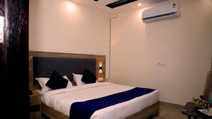 A hotel room with a large bed, a bedside table, a nightstand, a wall-mounted air conditioner, and a small table with a chair. - Lyf Corporate Suites - Noida Sector 19 (Noida)