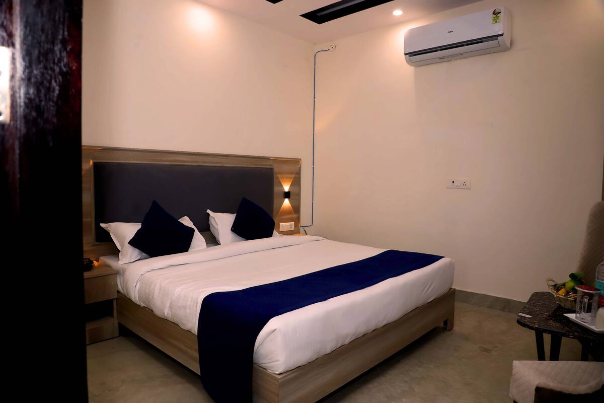 Ein Hotelzimmer mit einem großen Bett, einem Nachttisch, einer Wandklimaanlage und einem kleinen Tisch mit einem Stuhl.