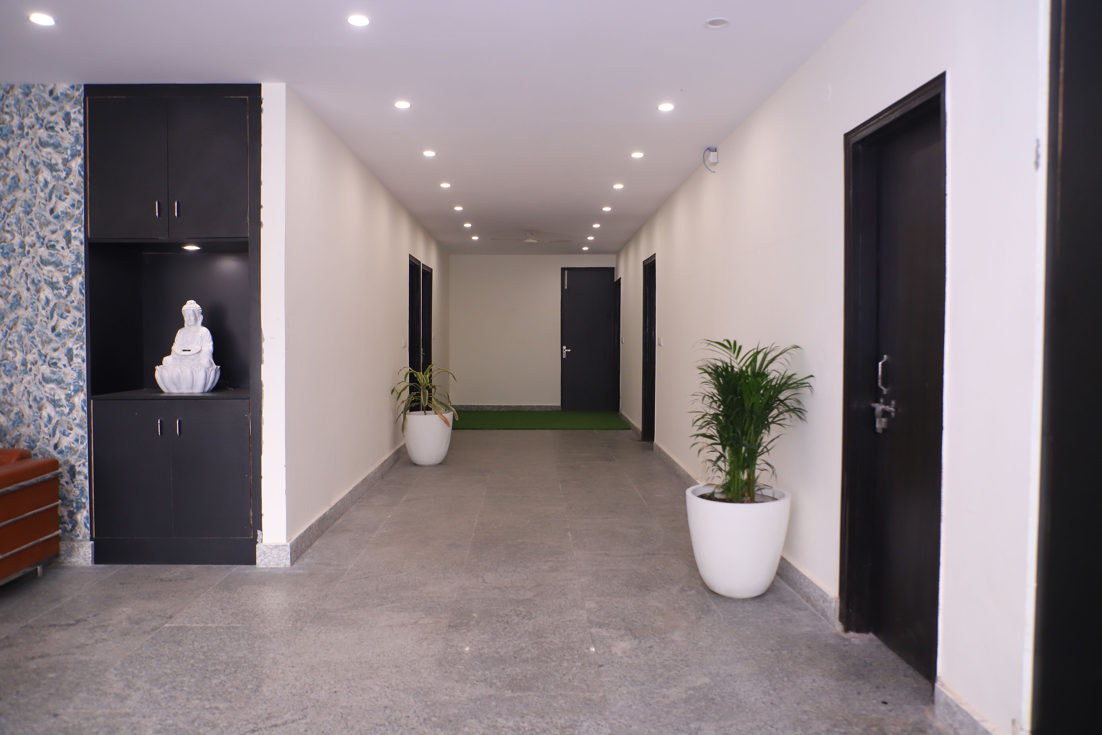 A hallway with a statue, potted plants, and black doors.