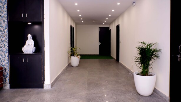 A hallway with a statue, potted plants, and a black cabinet. - Lyf Corporate Suites - Noida Sector 19 (Noida)