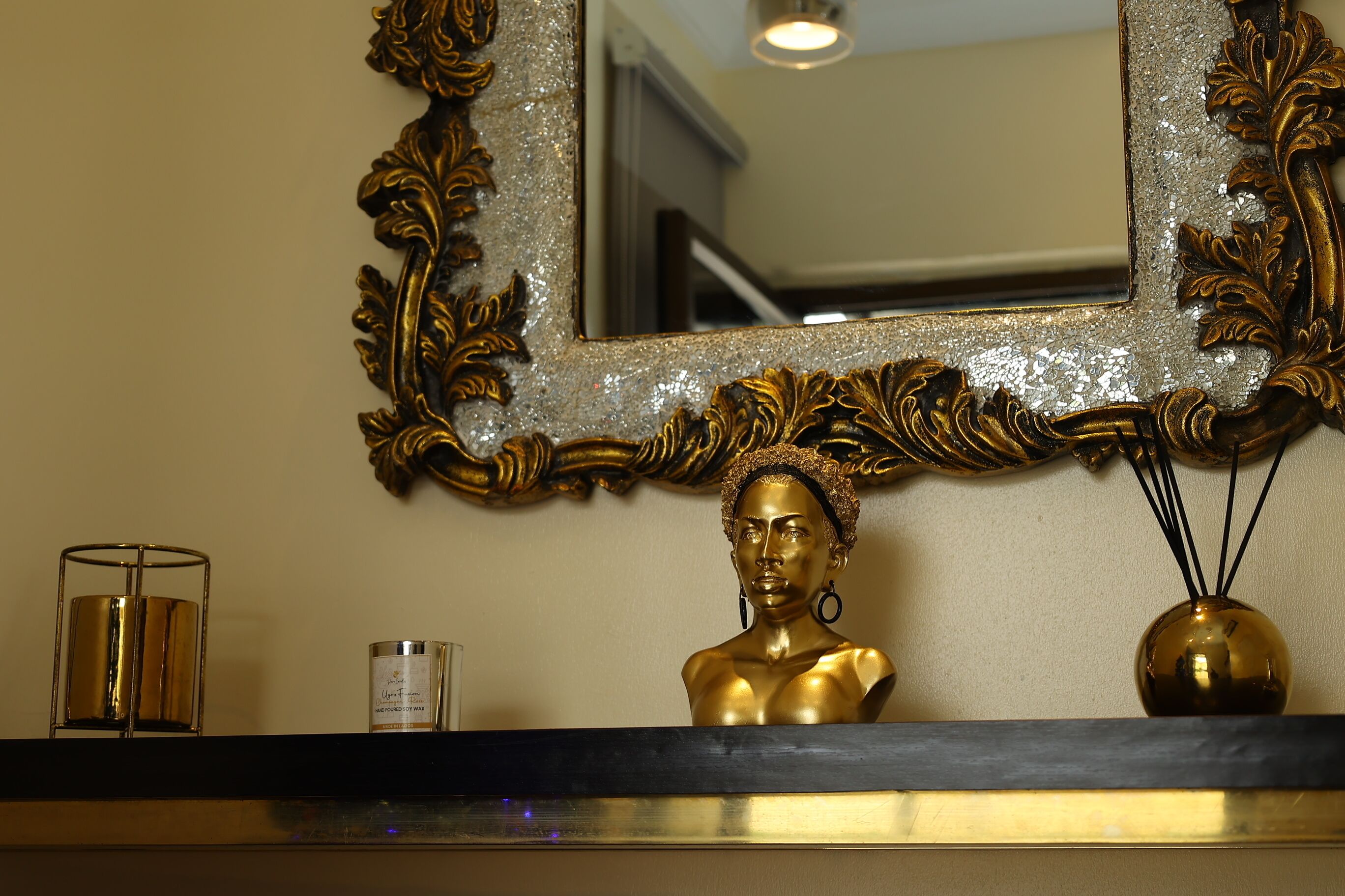 A gold bust on a shelf, a mirror with an ornate frame, and a candle.