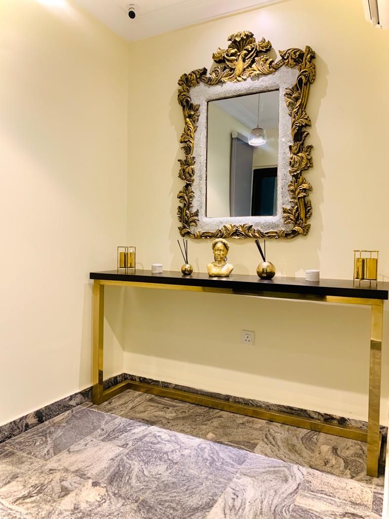 Un baño con piso de mármol, un espejo con marco dorado y un mostrador negro con base dorada.