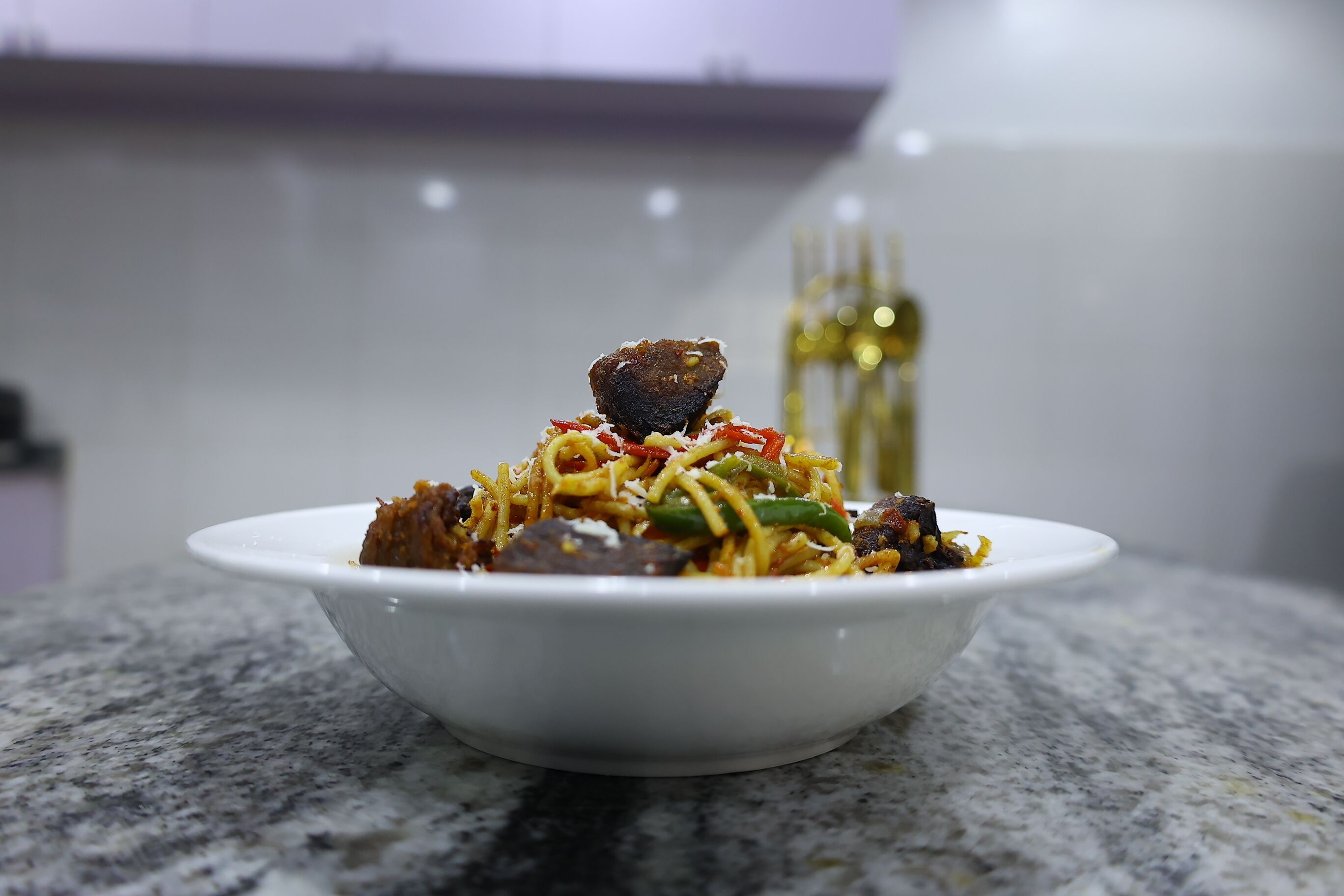 A bowl of noodles with vegetables and meat on a marble countertop.
