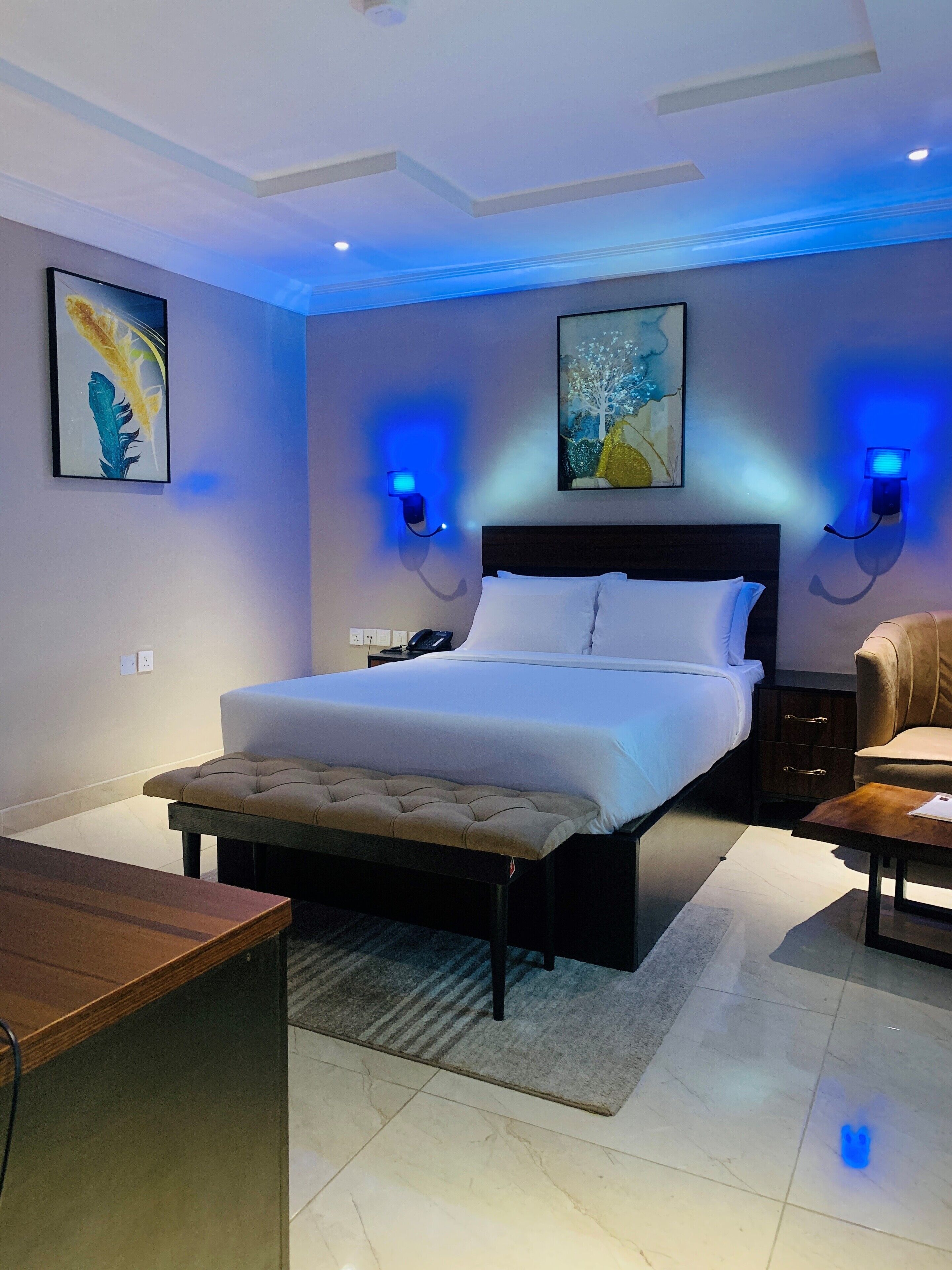 A modern bedroom with a large bed, bedside tables, a chair, and artwork on the walls.