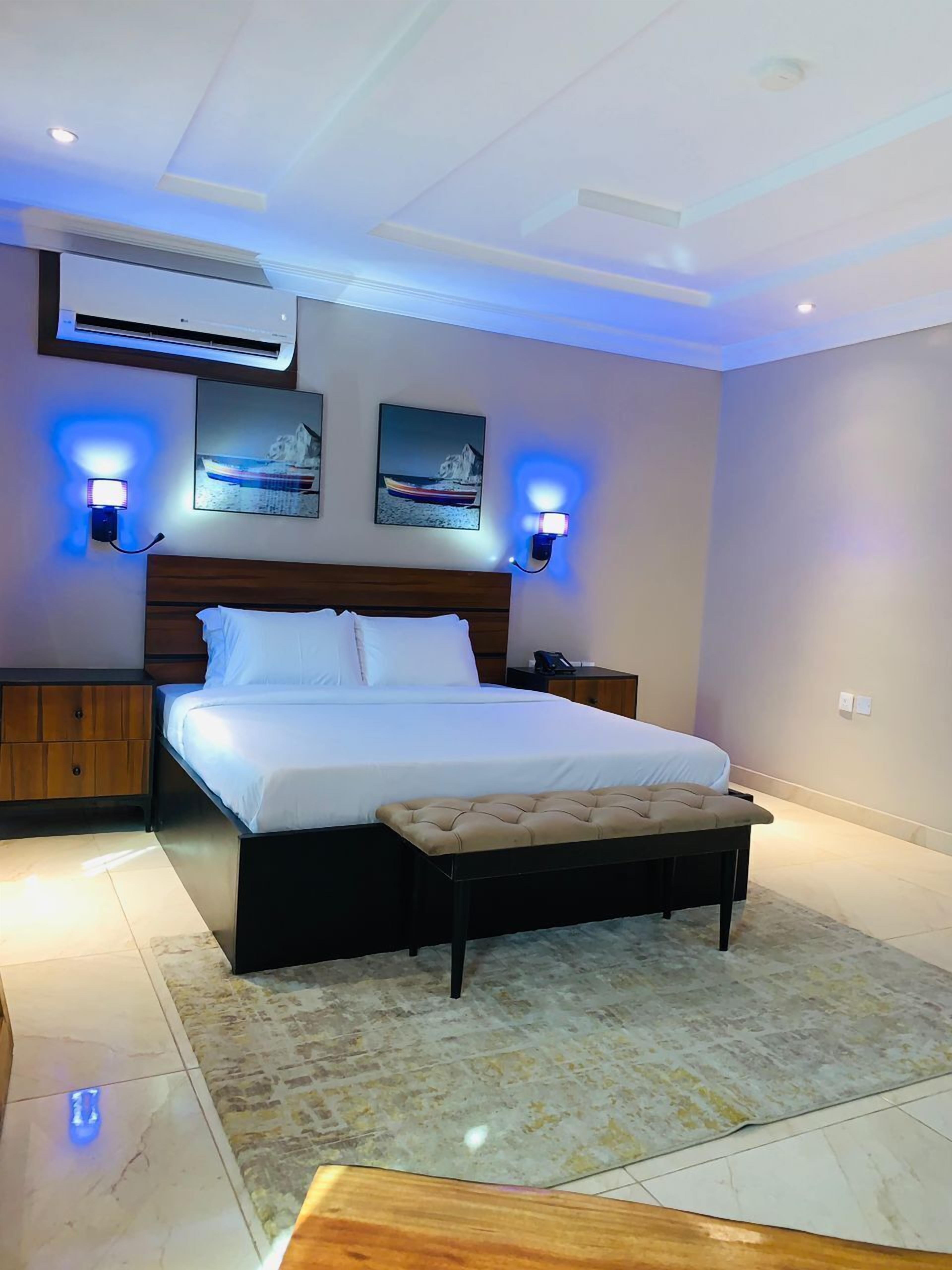 A modern bedroom with a large bed, bedside tables, an air conditioning unit, and wall-mounted lighting.