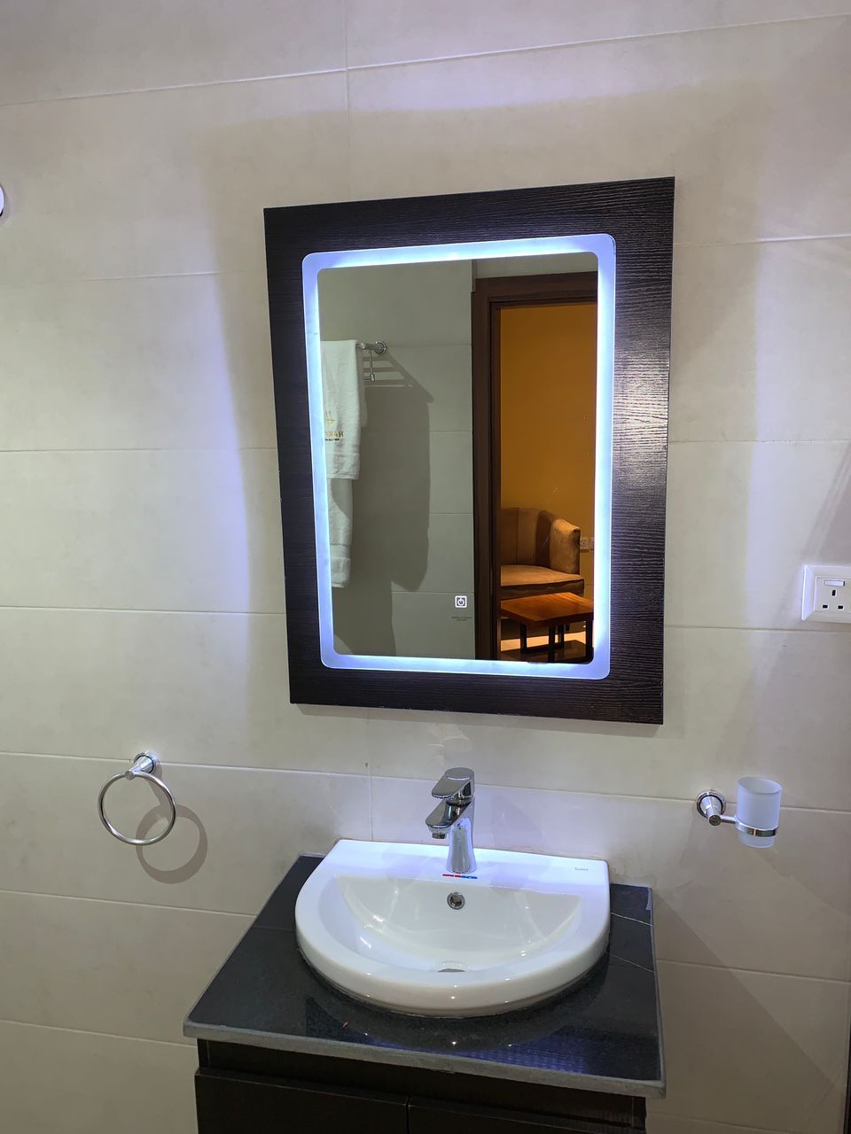 A bathroom with a white sink, a mirror with a light, and a towel ring.