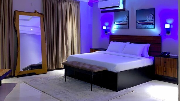 A modern hotel room with a large bed, a bedside table, a wardrobe, and a mirror.