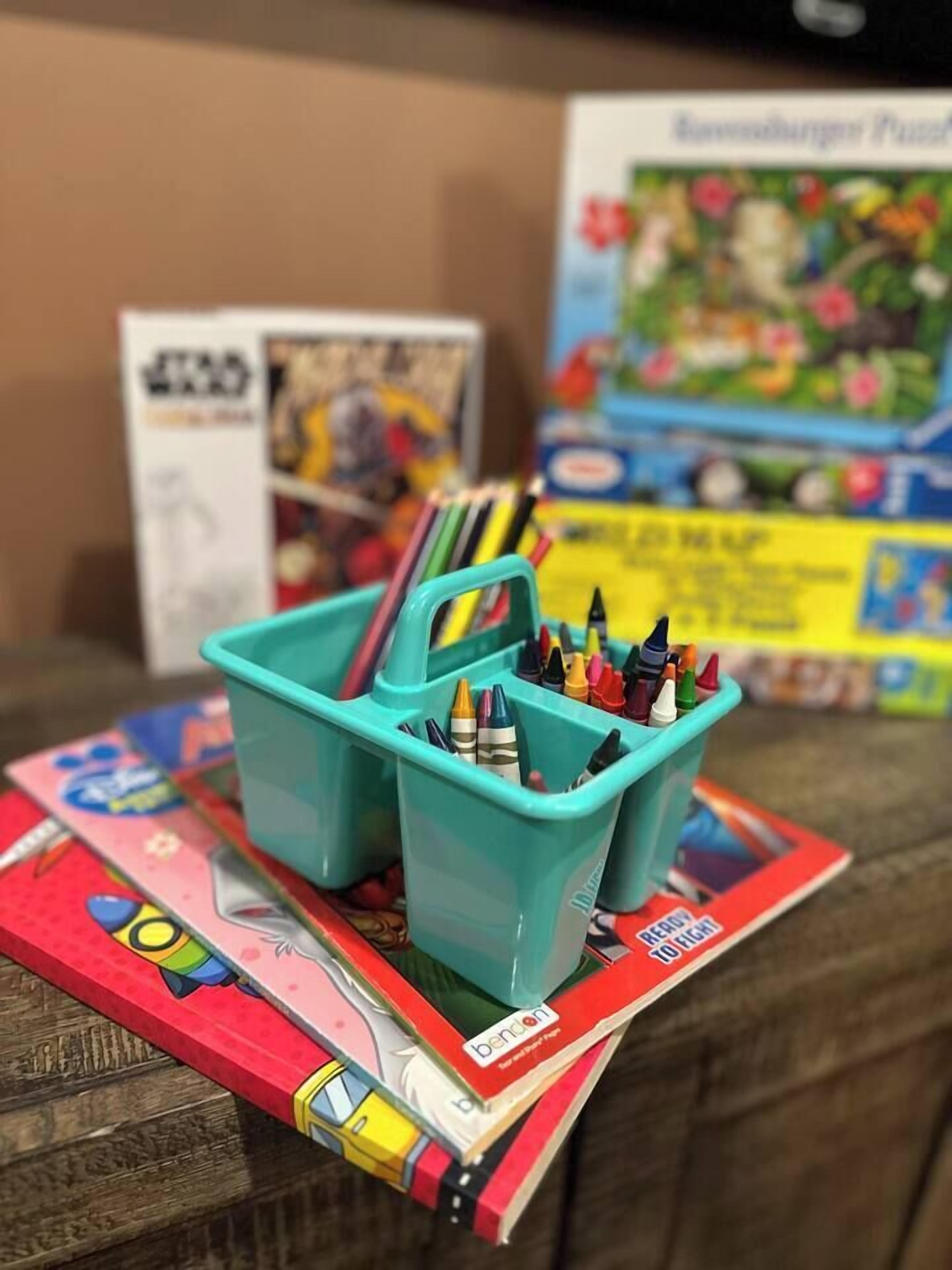 A teal container holding crayons and markers on a table with a book titled "Ready, You Fight!"