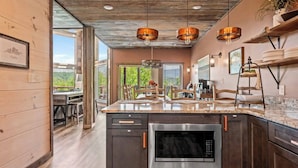 A modern kitchen with dark cabinetry, a stainless steel oven, and a large island with a built-in microwave. - Luxury Pool Cabin - Spectacular Fall Views - Close to Everything (Gatlinburg)
