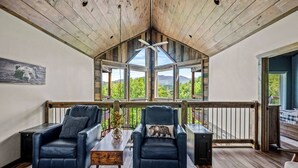 A cozy room with a wooden ceiling, two leather chairs, a small table, and large windows offering a view of greenery and mountains. - Luxury Pool Cabin - Spectacular Fall Views - Close to Everything (Gatlinburg)