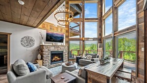 A spacious living area with a fireplace, comfortable seating, and large windows offering a view of the outdoors. - Luxury Pool Cabin - Spectacular Fall Views - Close to Everything (Gatlinburg)
