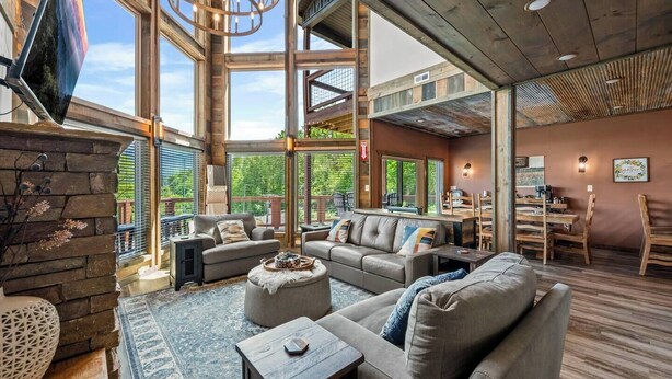 A spacious living area with a large sofa set, a fireplace, and a dining area with wooden furniture. - Luxury Pool Cabin - Spectacular Fall Views - Close to Everything (Gatlinburg)