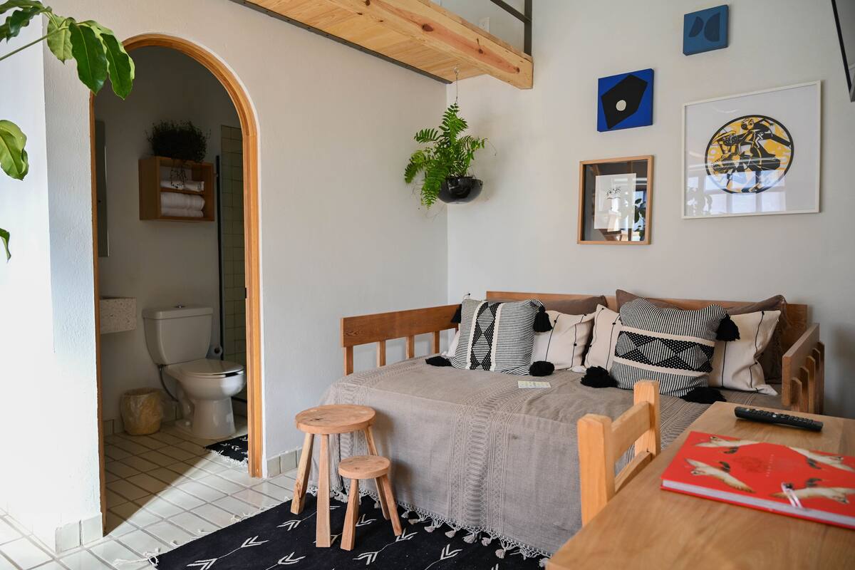 Une chambre confortable avec un lit, une table de chevet et un petit tabouret. On aperçoit une salle de bain à travers une arche.
